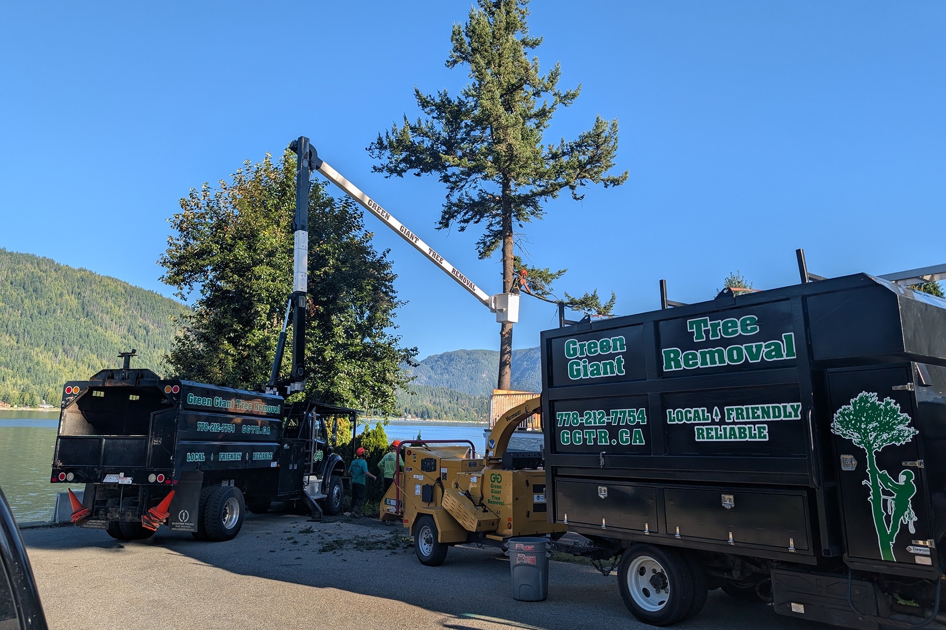Using crane in between two green giant tree removal trucks